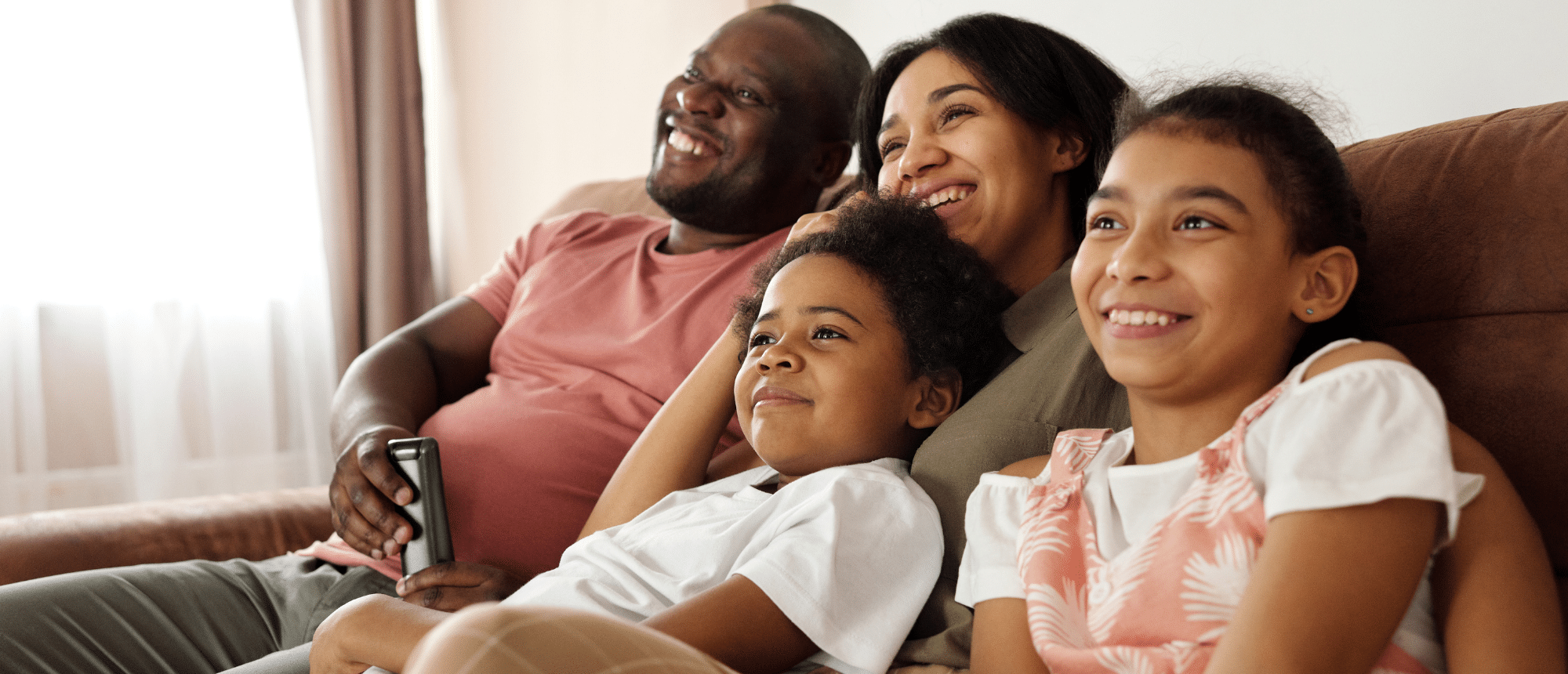 Happy family on a couch in front of windows.