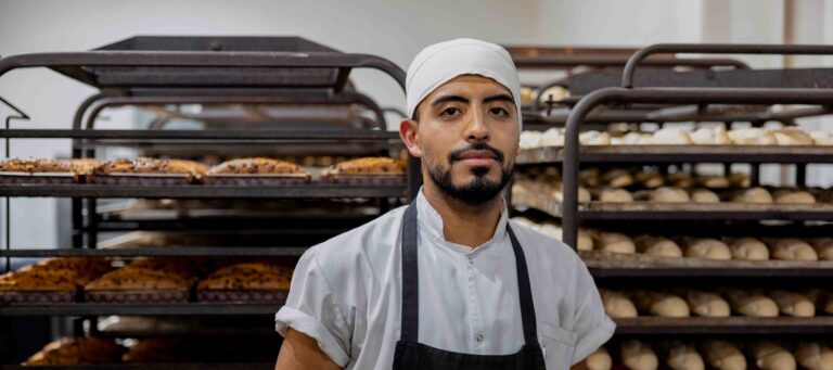 Baker stands in front of trays loaded with bread loaves.